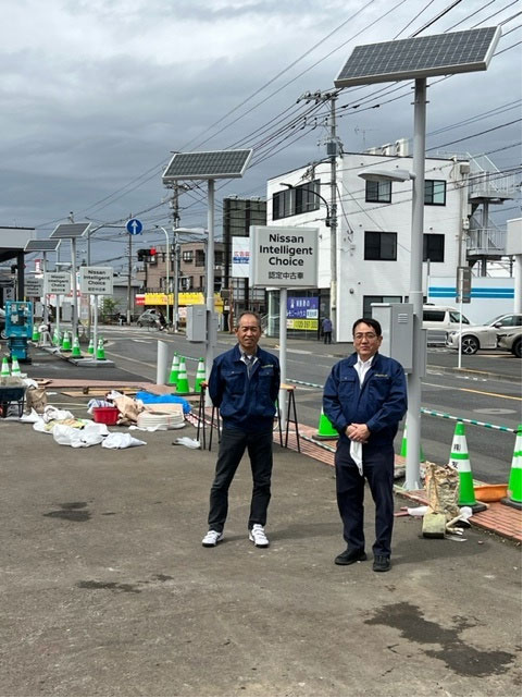 写真）日産東京販売株式会社に納品された非常用蓄電池付き太陽光外灯（４灯）　右が加東社長