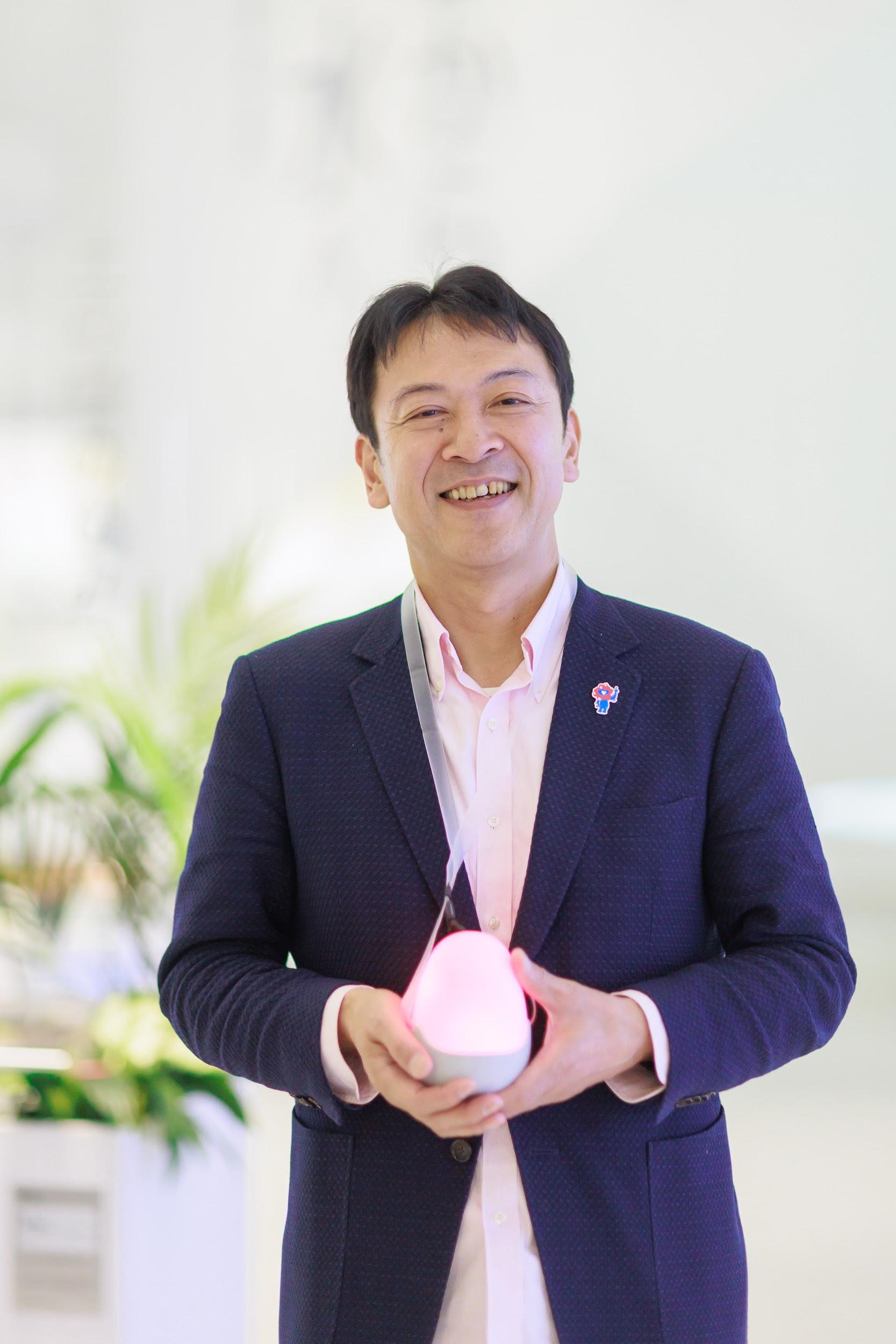 写真)タマゴ型デバイスを手に持つ岡田館長